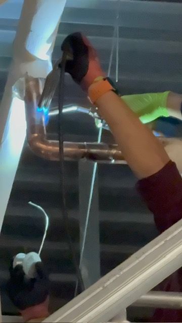 Person in a safety harness working on a metal structure with a tool, viewed from below