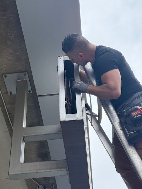 Technician leaning into an electrical panel on a metal ladder in an industrial setting