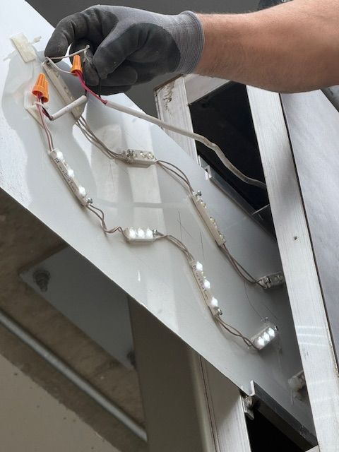 Gloved hand wiring LED light strips on a metal panel in a workshop