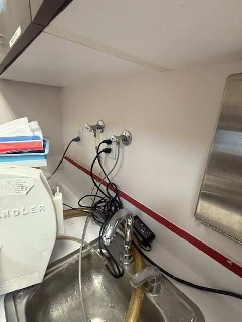 Kitchen sink under countertop with exposed plumbing, hoses, and a red wall stripe.