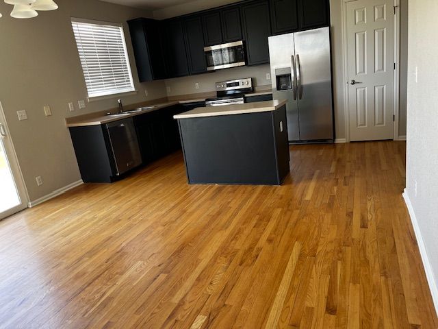 Empty modern kitchen with dark cabinets, stainless appliances, and hardwood floors