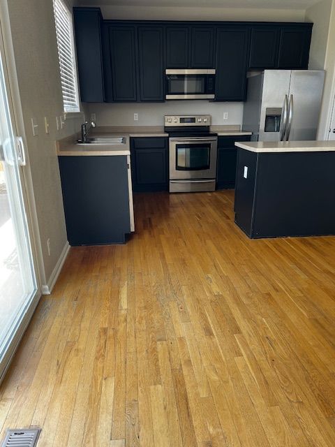 Empty modern kitchen with dark cabinets, stainless steel appliances, and wood flooring