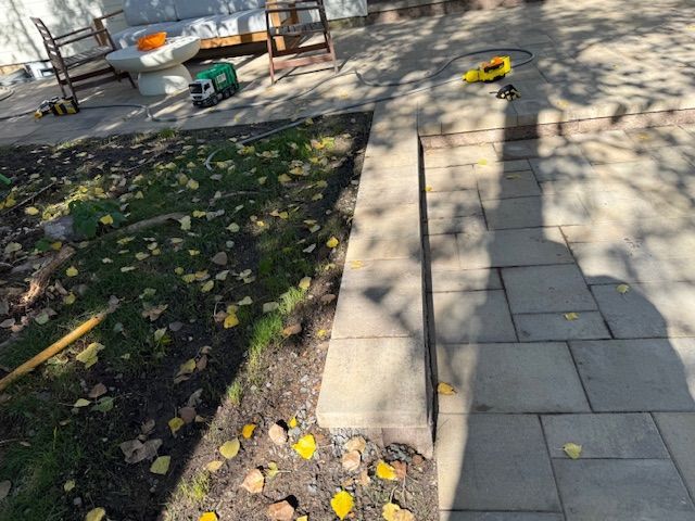 Tree-lined park path with stone pavers, fallen leaves, and benches in sunlight