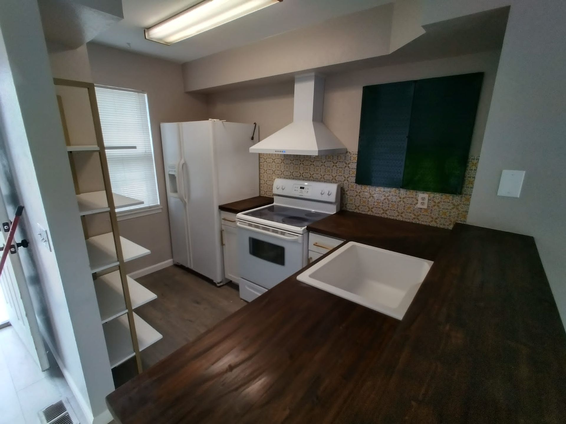 Small kitchen with white appliances, dark countertops, open shelving, and a window above the sink.