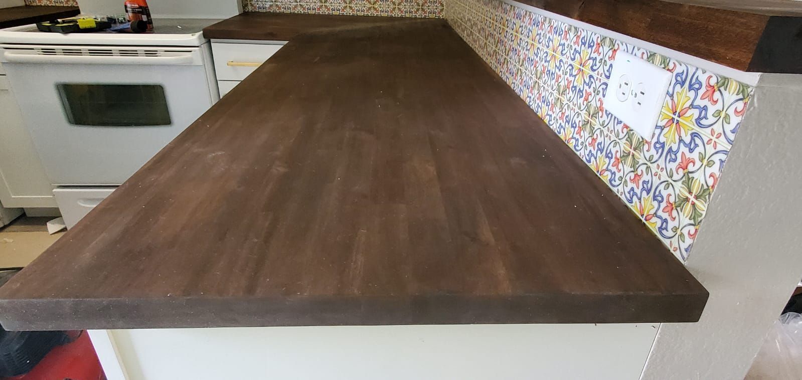 Long dark wood countertop in a kitchen with white cabinets and patterned tile backsplash
