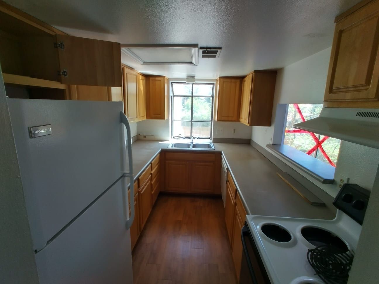 Narrow kitchen with wood cabinets, white countertops, stainless fridge, and a window over the sink.