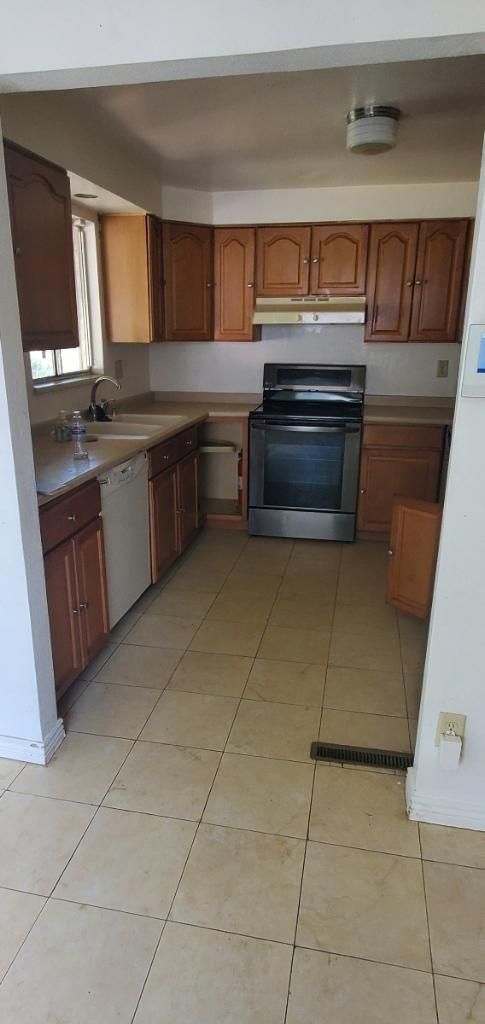 Small kitchen with wooden cabinets, black stove, beige tile floor, and a doorway in the foreground