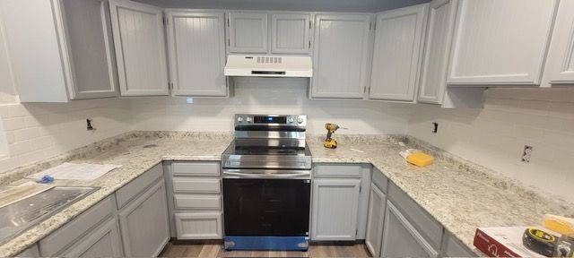 Empty white kitchen with gray cabinets, speckled countertops, and a black stove centered under a range hood.