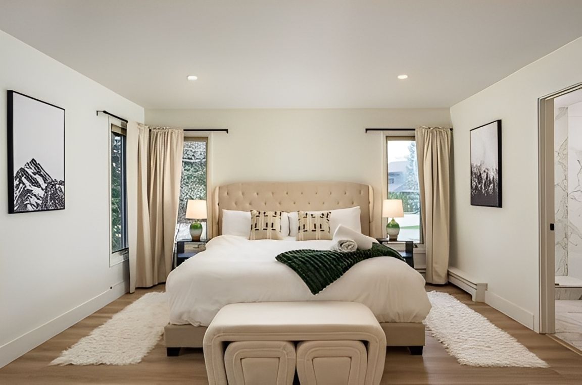 Bright, modern bedroom with a large bed, beige decor, and framed wall art on both sides.