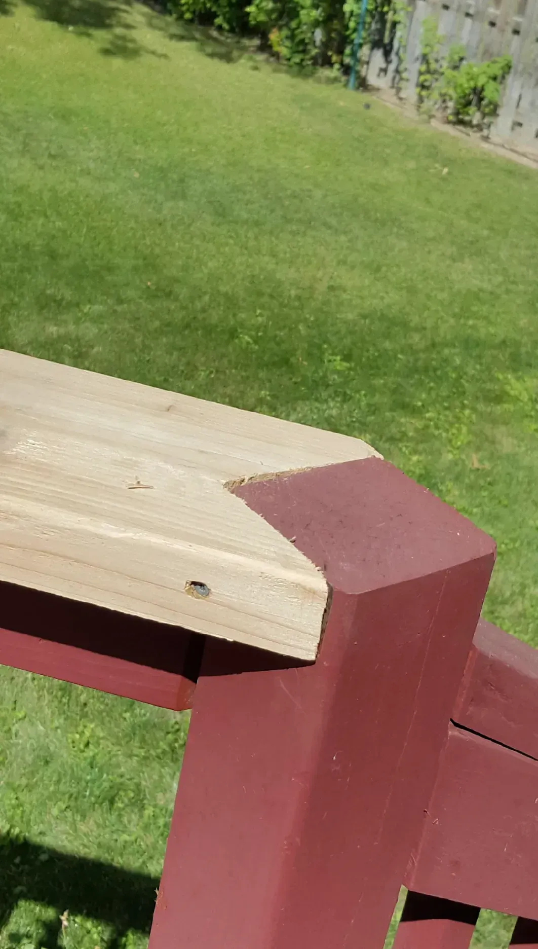 Wooden porch railing painted red with a light wood top, beside a green lawn.