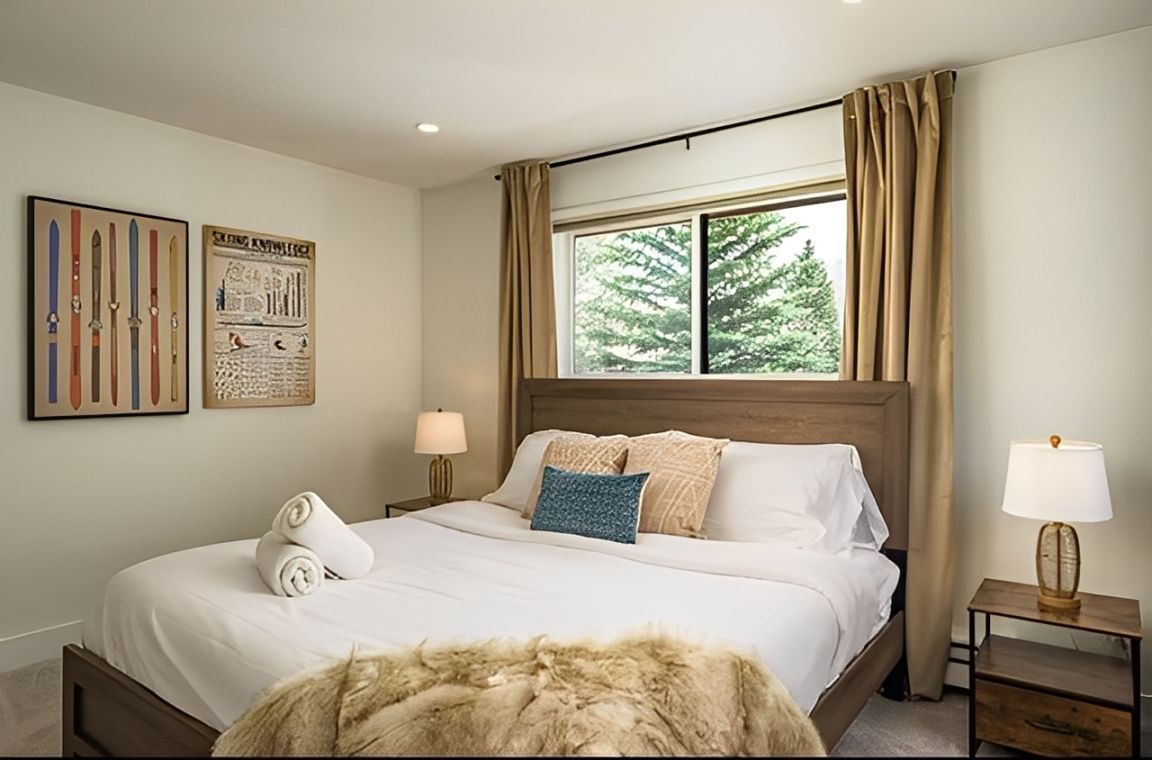 Cozy bedroom with a queen bed, beige decor, bedside lamps, and a window with curtains.