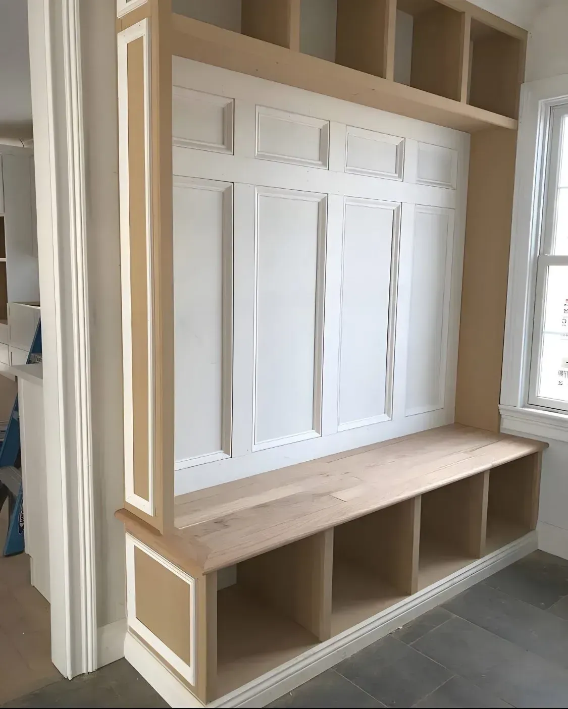 White built-in bench and paneled wall cabinet in a room under construction