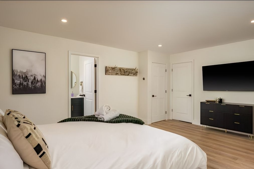 Bright minimalist bedroom with a bed, wall art, mirrored closet, and TV on a dresser