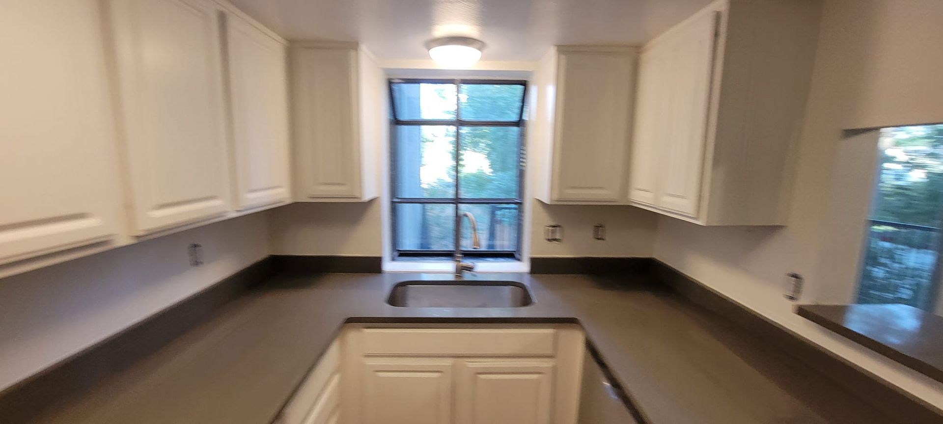 Bright galley kitchen with white cabinets, dark countertops, and a window over the sink.