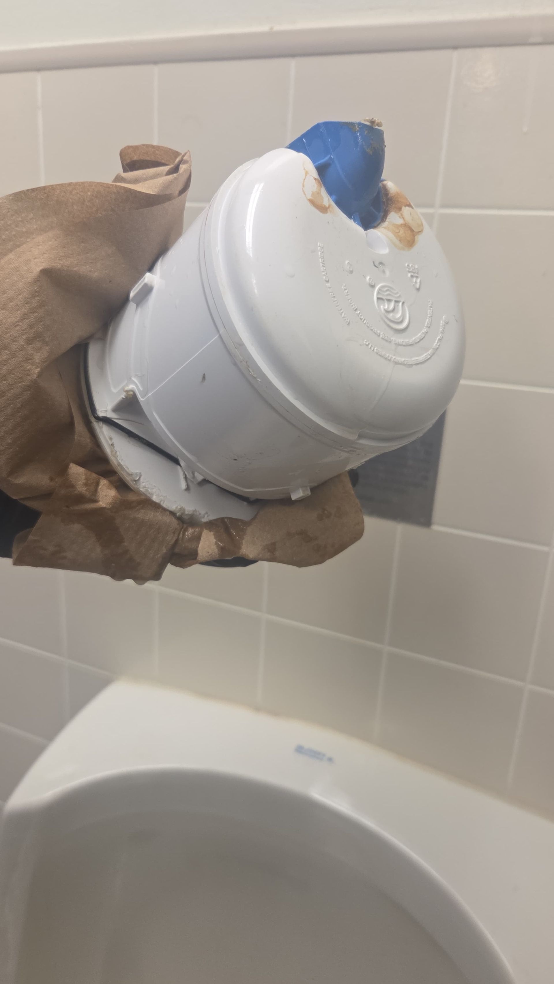 Broken white toilet tank held with cardboard and blue tape above a toilet bowl in a tiled bathroom