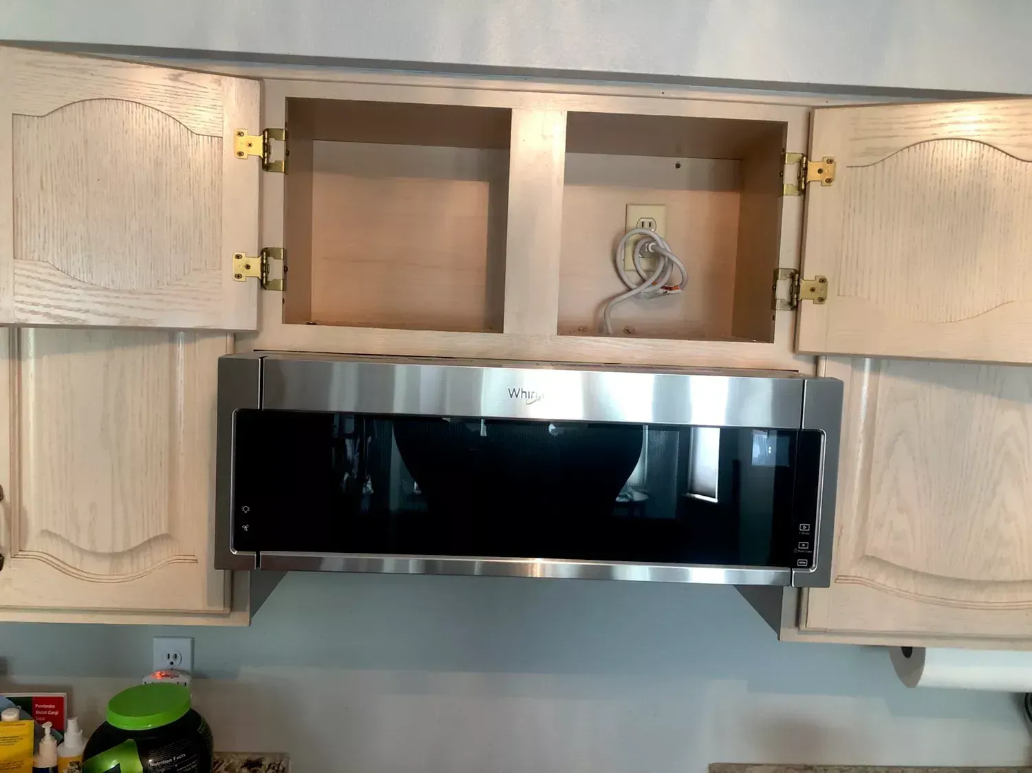 Kitchen cabinets above a black microwave, with open upper cabinet doors and a small decorative jar inside