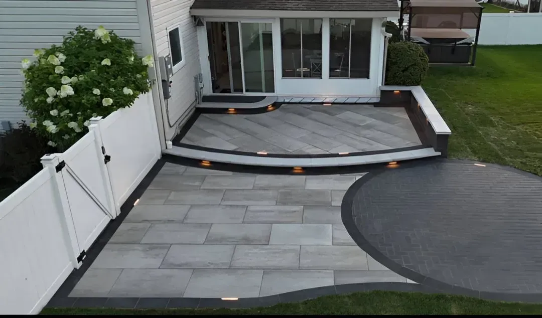 Backyard patio with gray pavers, curved dark border, white fence, and house sliding doors.