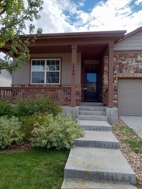 Front porch with steps leading to a beige house and garage, with shrubs and a green lawn.