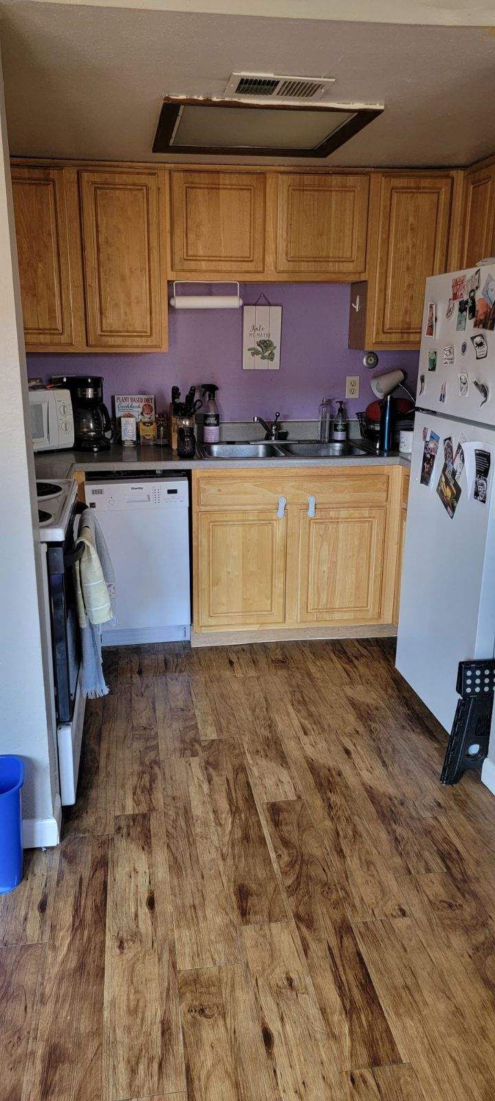 Small kitchen with oak cabinets, purple walls, white appliances, and wood-look flooring.