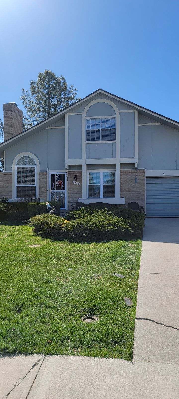 Suburban house with a front lawn, arched windows, and a driveway under a clear blue sky