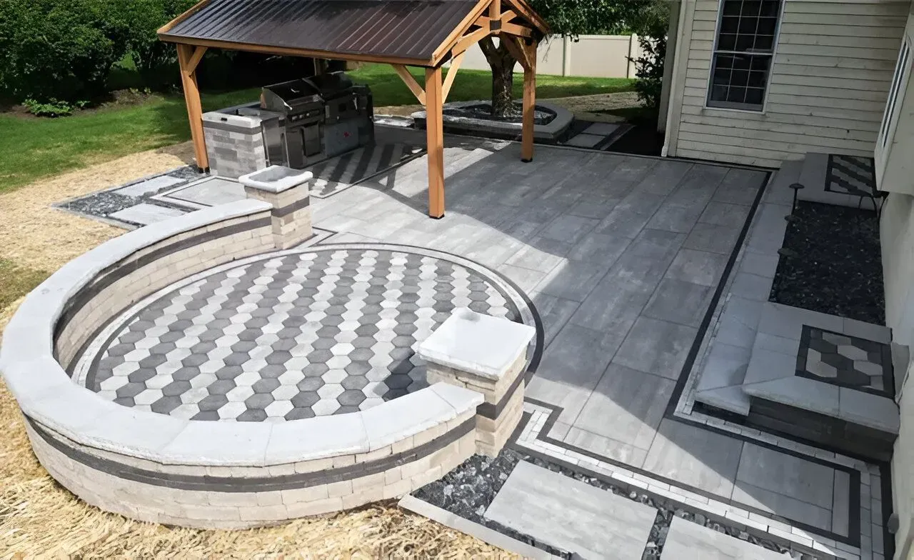 Backyard patio with a circular patterned fire pit and stone seating under a wooden shelter