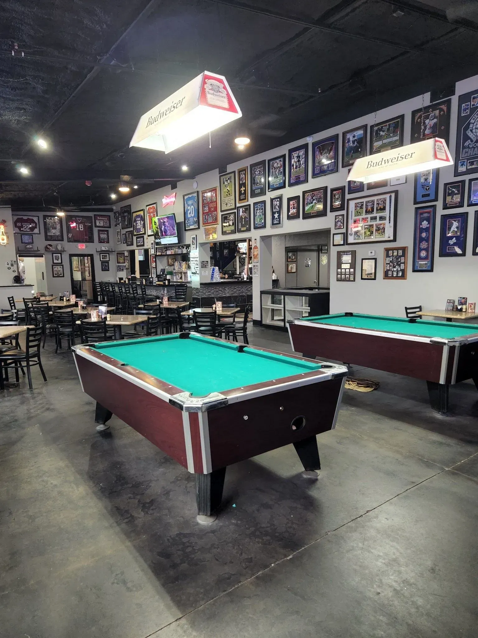 Pool hall with two green-felt billiards tables, framed wall art, and overhead lights