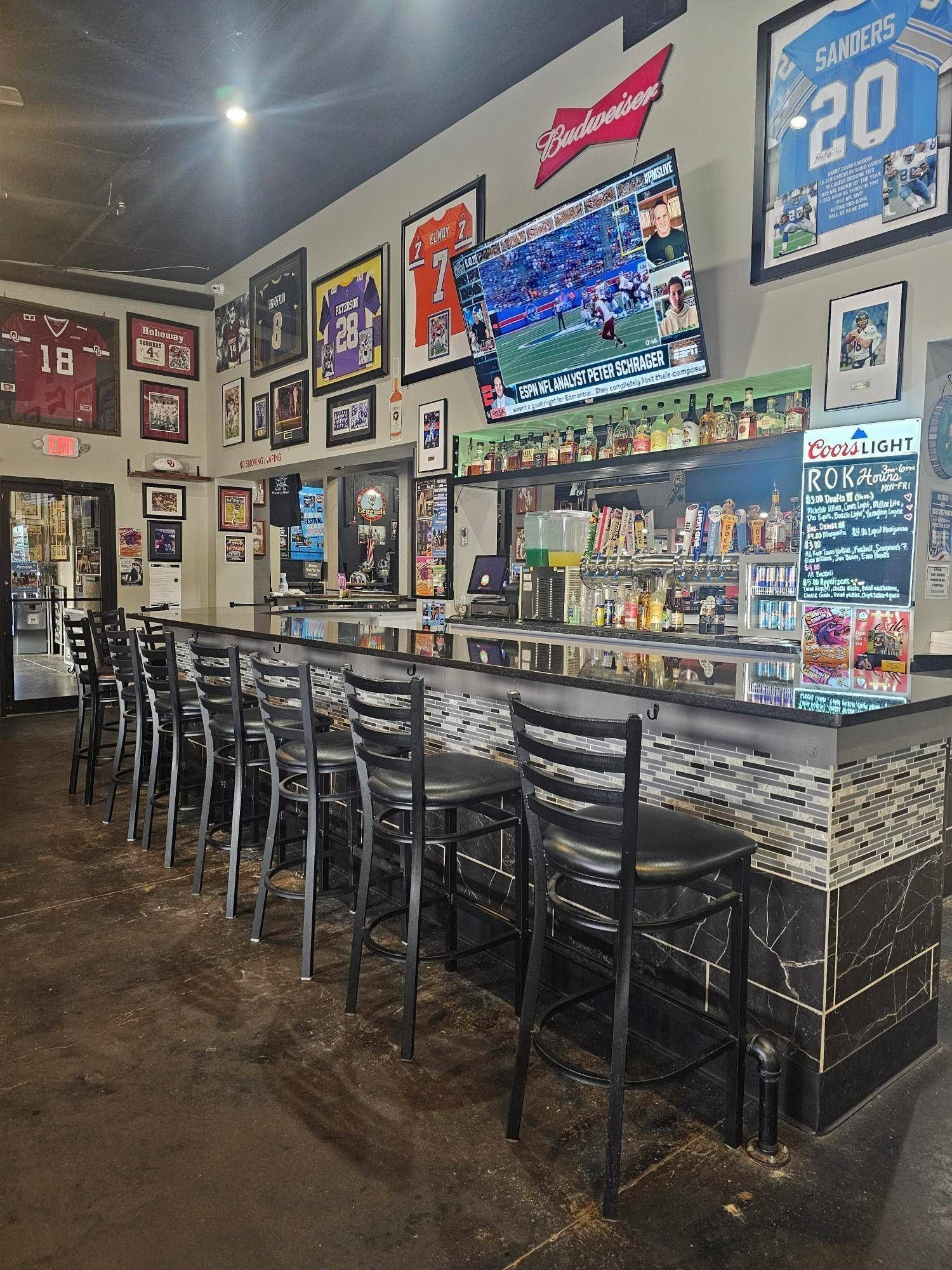 Sports bar interior with long marble bar, black stools, TVs, and framed jerseys on the walls