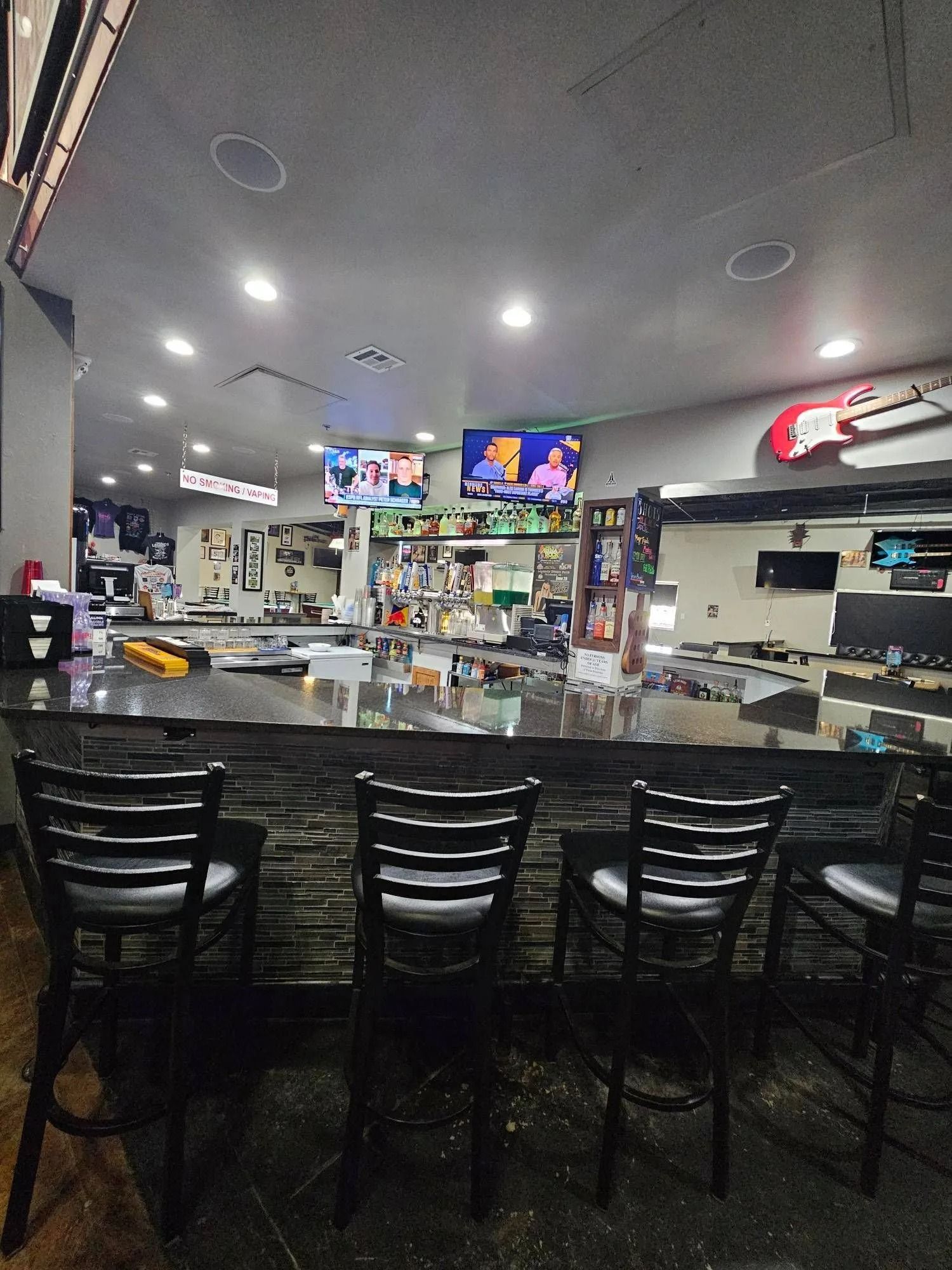 Empty restaurant bar with black stools, TVs, and a gray ceiling under bright lights