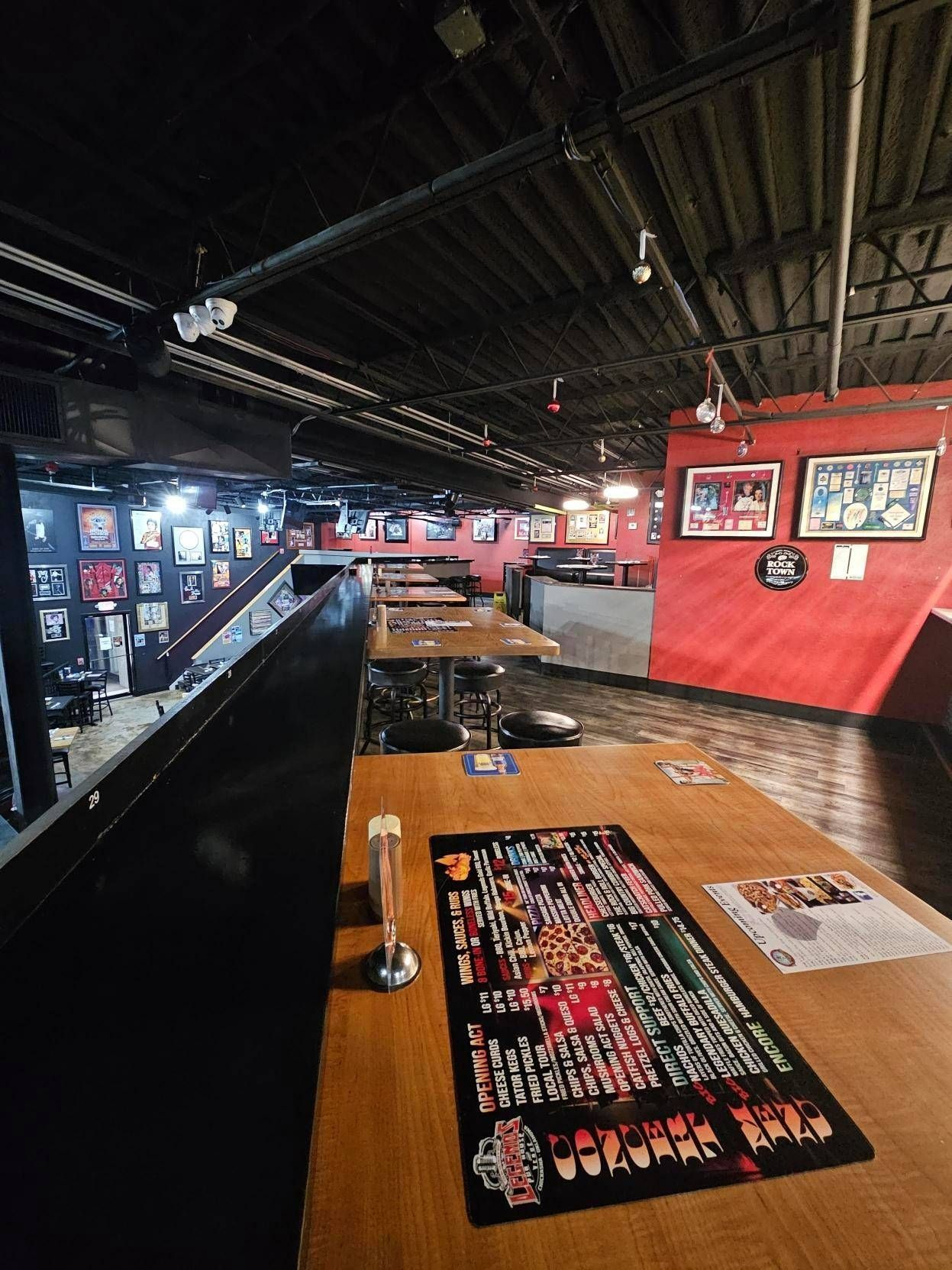 Empty bar interior with long wooden tables, black ceiling, and red walls displaying framed photos.