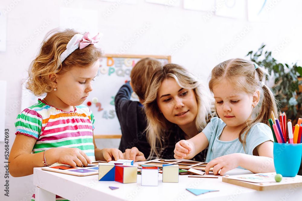 Two girls are playing while a teacher is watching them.