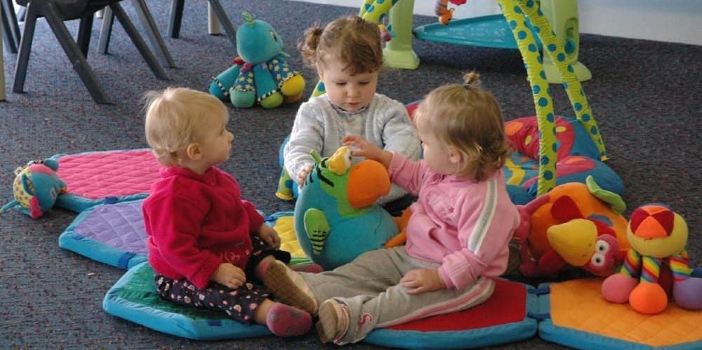 Three little girls are playing with stuffed animals in a room with the caption having fun with our friends