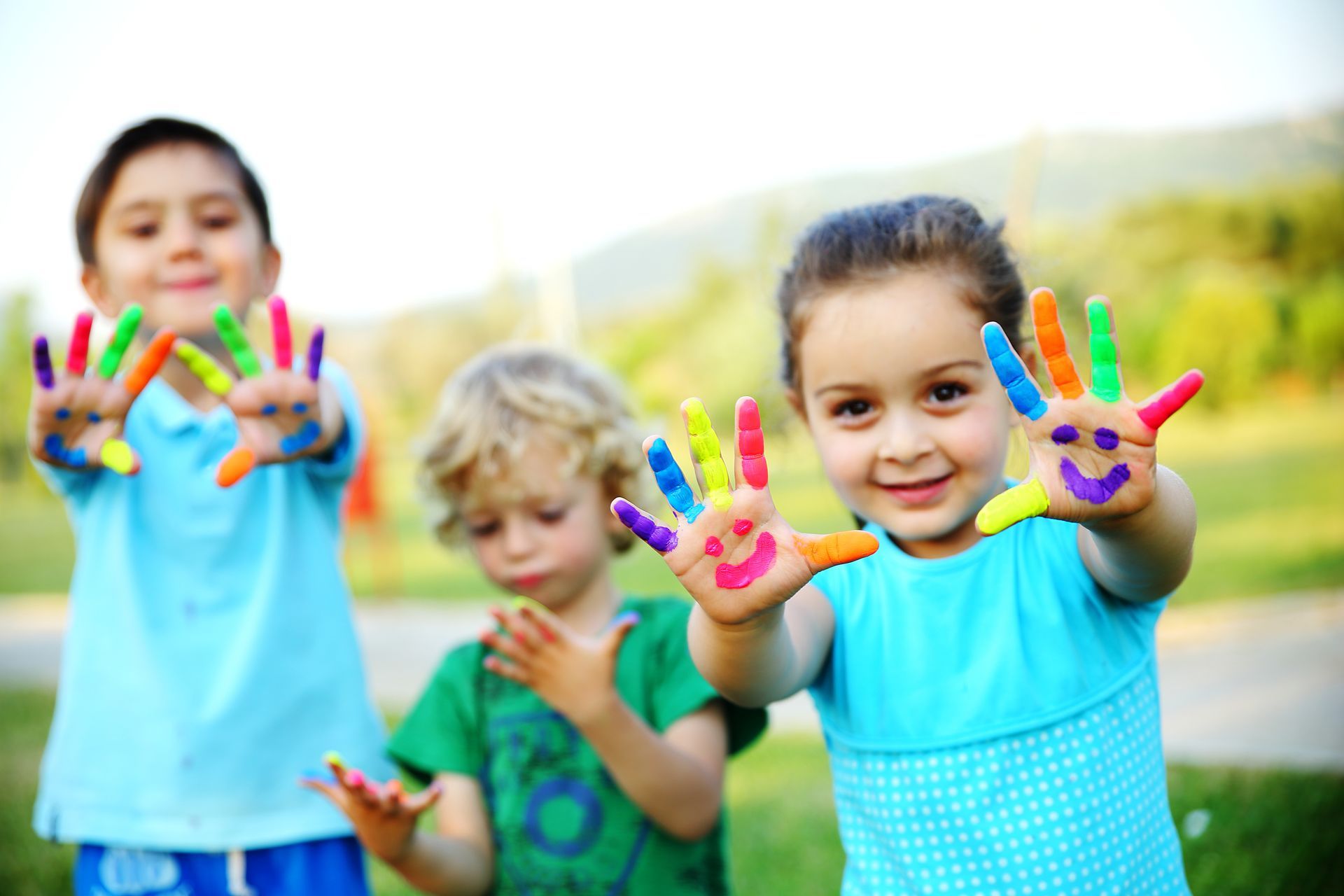 Three children holding up their hands with finger paint on their hands