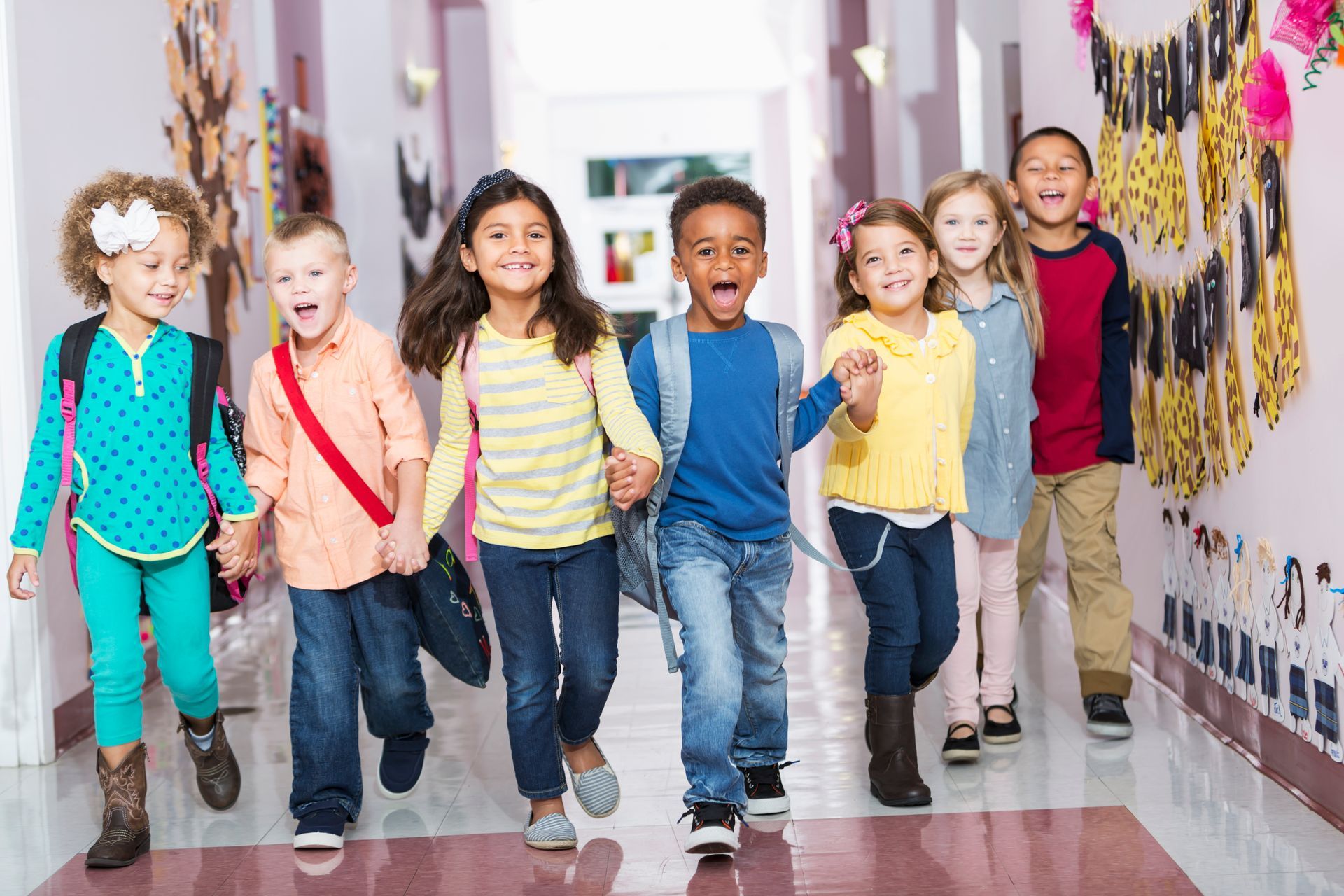 A group of children are walking down a hallway holding hands.