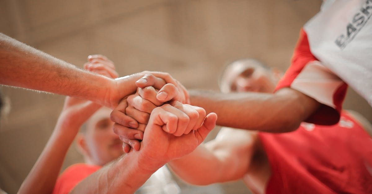 Hands stacked together in a team huddle, with people wearing red shirts.
