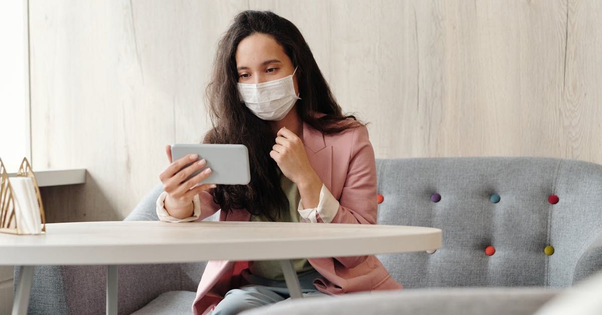 A woman wearing a mask is sitting at a table using a tablet.