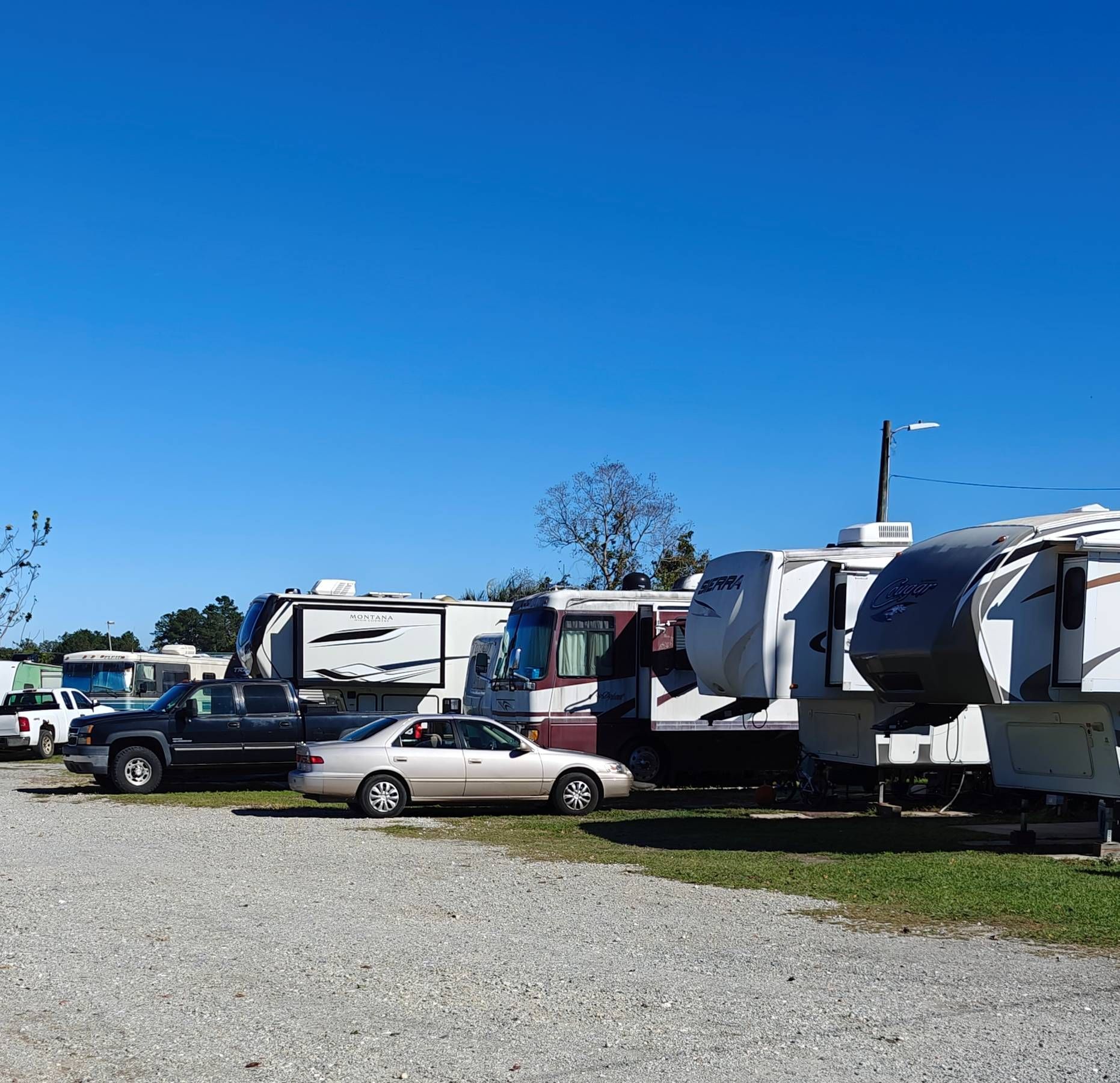A row of rvs are parked in a gravel lot.