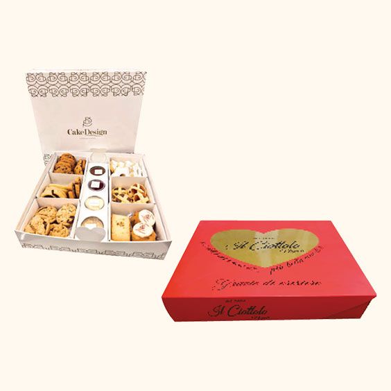 Confezioni regalo di pasticcini assortiti, tra cui una scatola a tema cuore rosso e una scatola aperta con vassoio color crema.