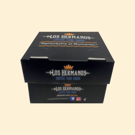 Scatola di caffè Los Hermanos nera con logo dorato su sfondo beige.