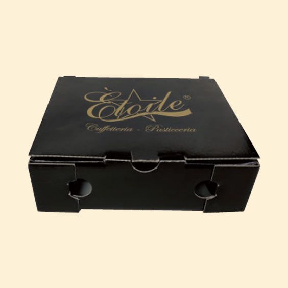 Scatola per pasticcini nera con logo dorato e manici intagliati su sfondo chiaro.