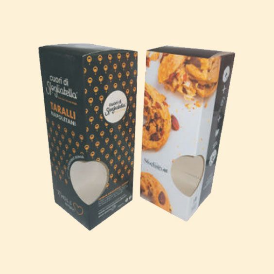 Due scatole decorative per snack, una nera con pois dorati e una bianca con biscotti arancioni, su sfondo color crema.