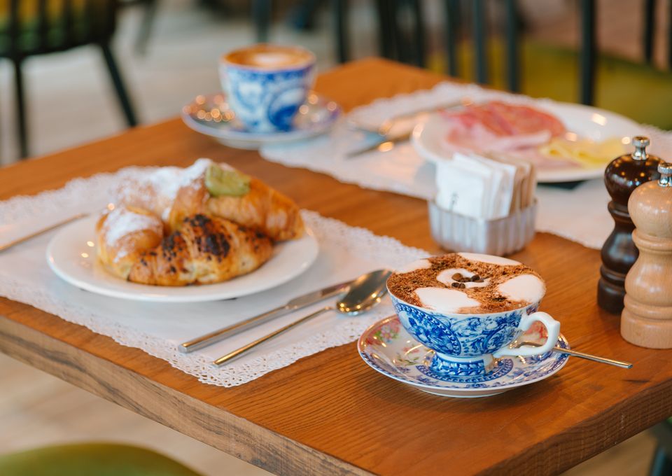 Bandeja de desayuno con café, bollería y platos sobre una mesa en una acogedora cafetería.