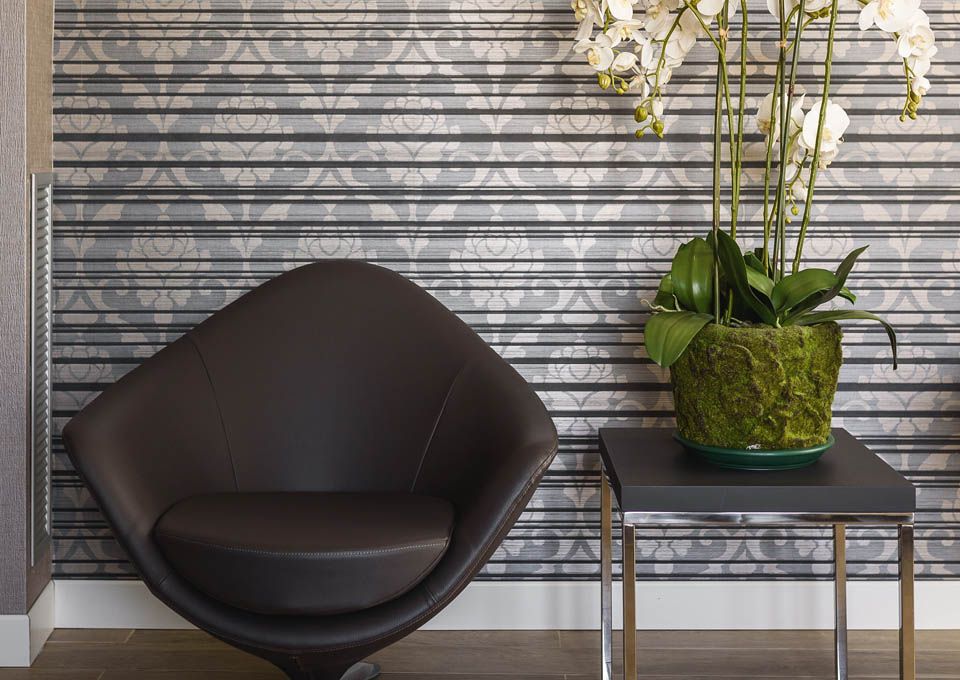Silla negra moderna junto a una mesita con una orquídea blanca contra una pared de rayas grises.