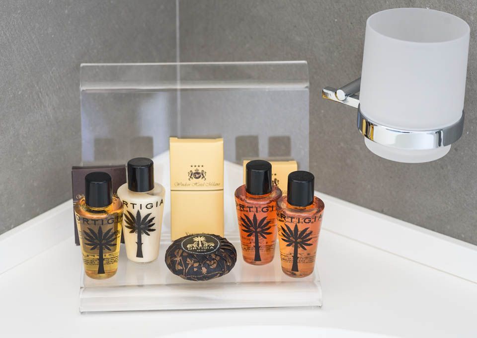 Expositor de perfumes de lujo con frascos dorados y negros sobre un soporte de acrílico transparente junto a un aplique