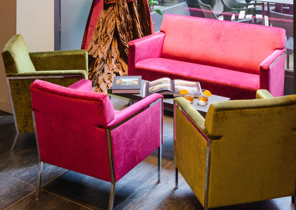 Sillones tapizados de colores y un sofá rosa dispuestos alrededor de una mesa pequeña en una zona de estar.