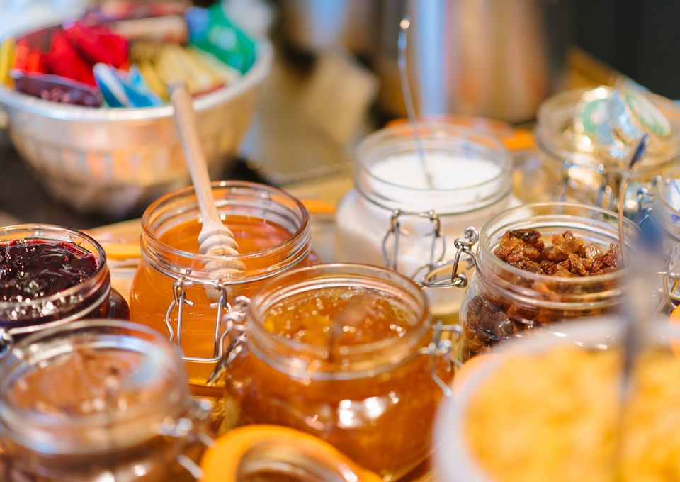 Frascos variados de mermelada, miel y conservas en una mesa de buffet.