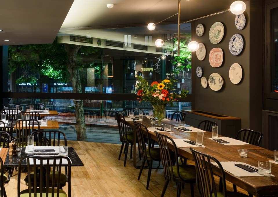Interior de restaurante moderno y acogedor con mesas de madera, sillas negras, relojes de pared e iluminación cálida.