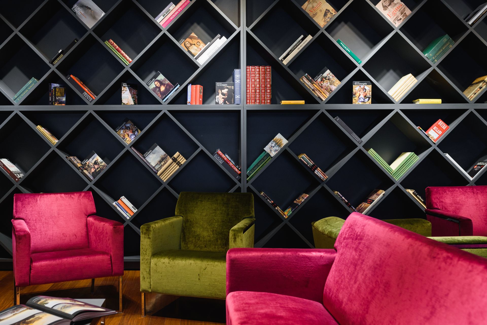 Sillones rosas y verdes en una sala de lectura con estanterías oscuras en forma de diamante.
