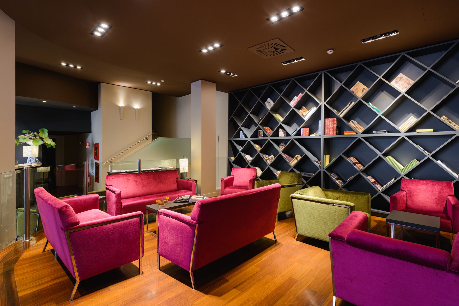 Salón moderno con sillas magenta, suelos de madera y una pared con botellero geométrico.