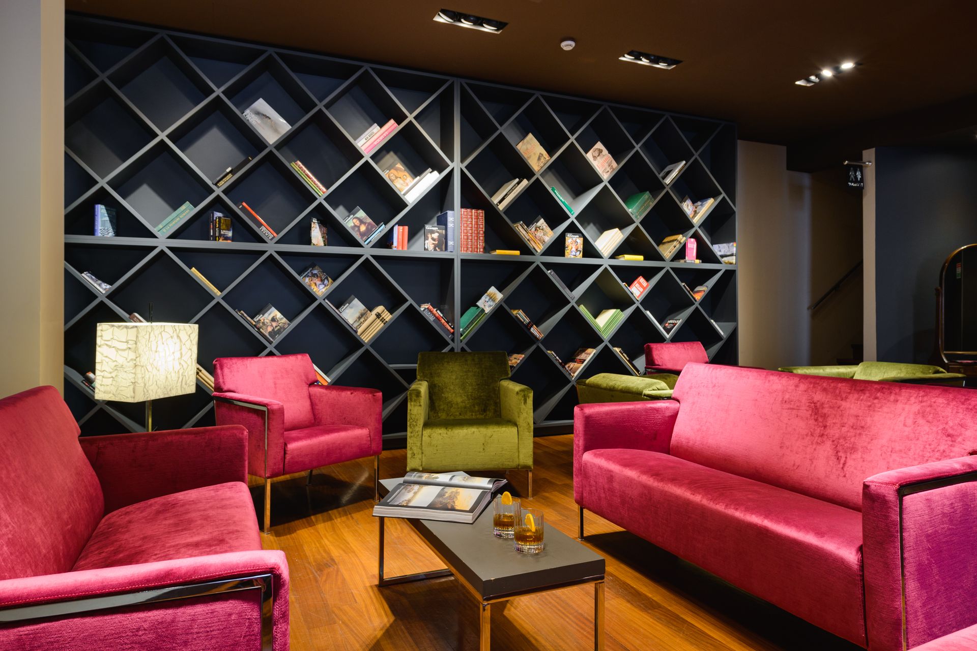 Elegante salón con sofás rosas, silla verde, mesa de madera y estantería con diseño de rombos.