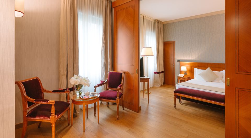Suite de hotel con zona de estar, suelos de madera y un dormitorio visible a través de una mampara abierta.